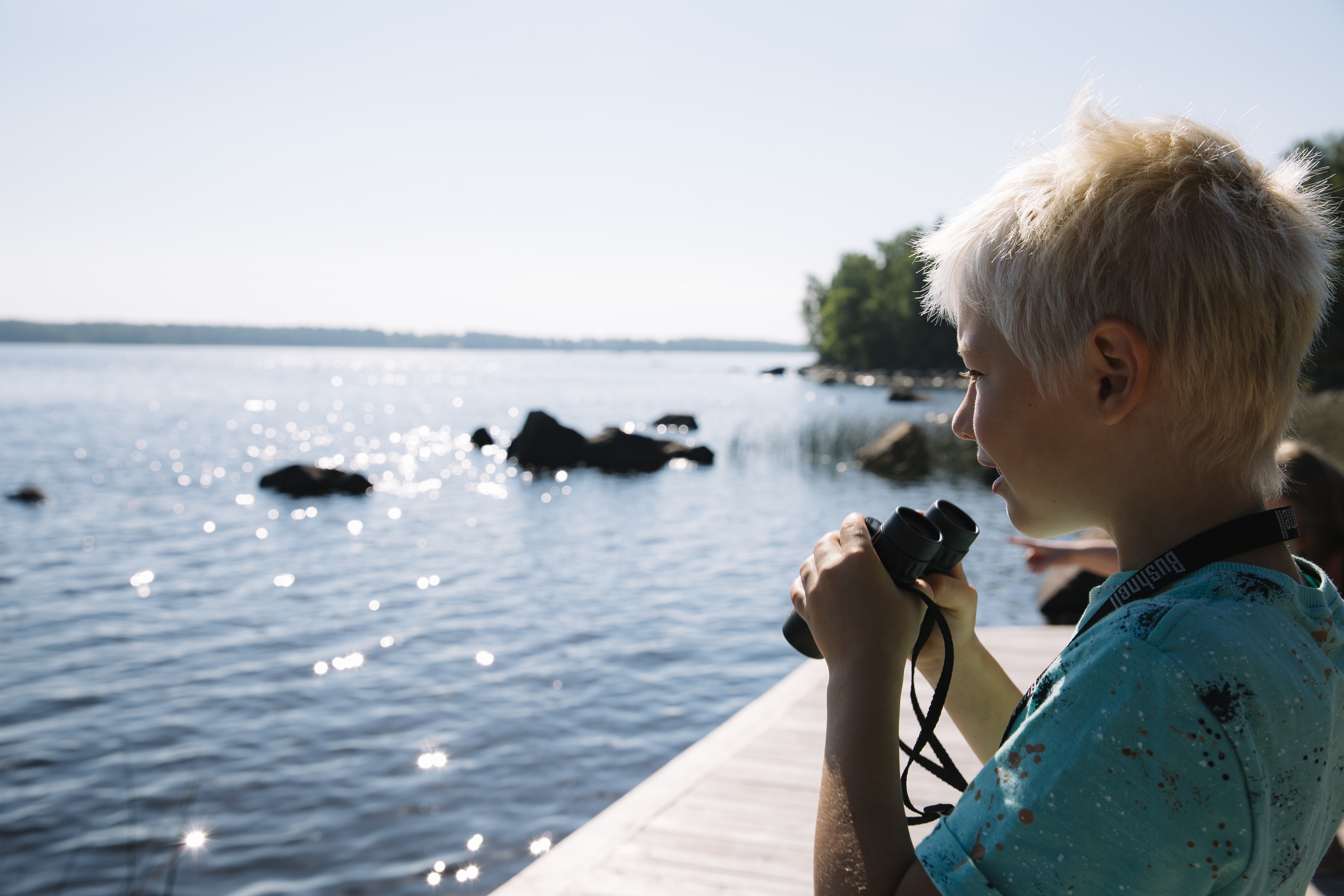 pojke står med kikare och tittar ut över en sjö