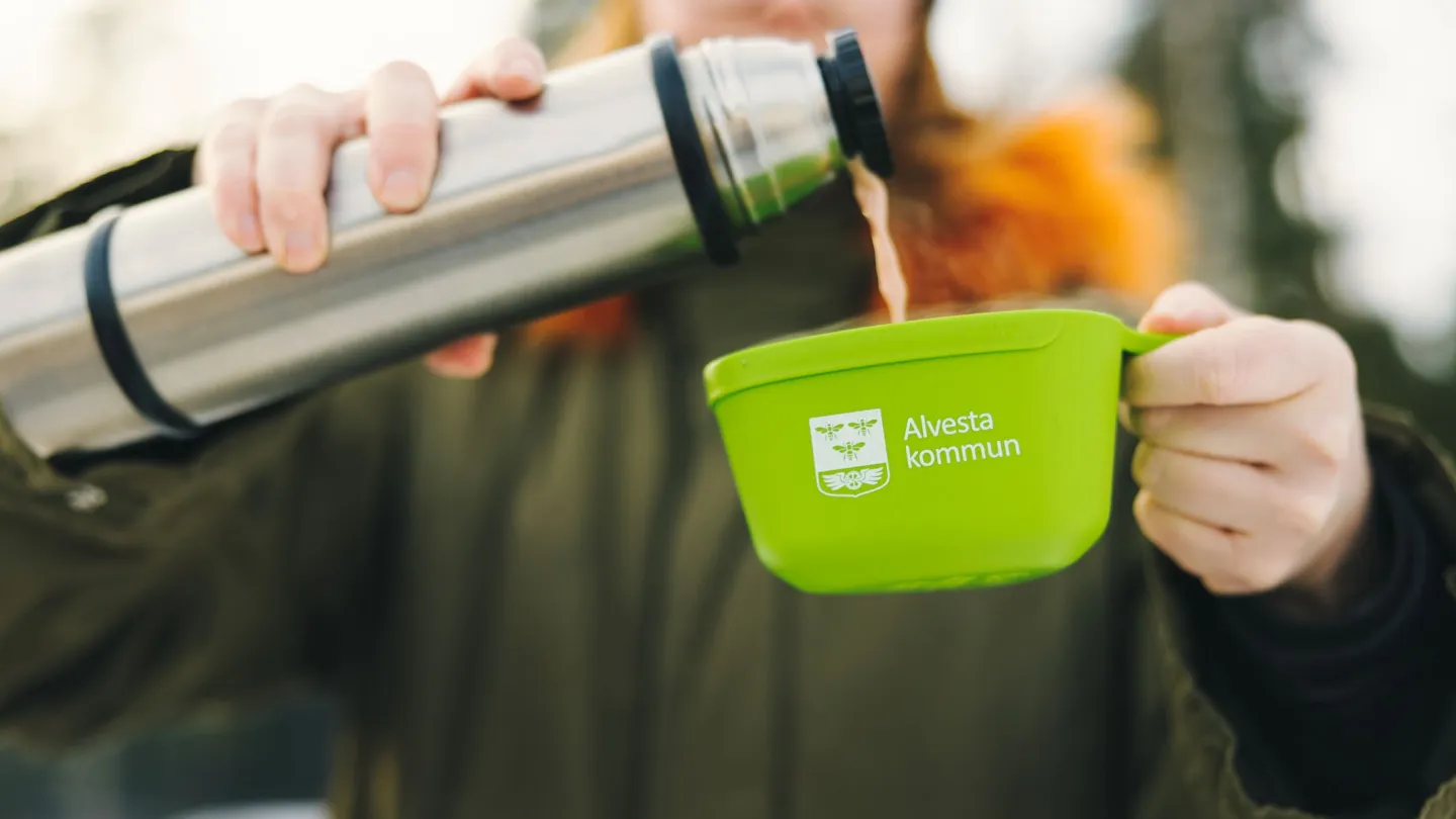 Kvinna häller varm dryck i en grön kåsa från en termos 