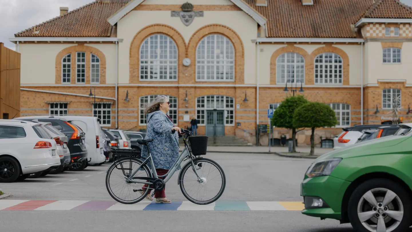 Kvinna går med cykel över färgglatt övergångsställe framför Alvesta station
