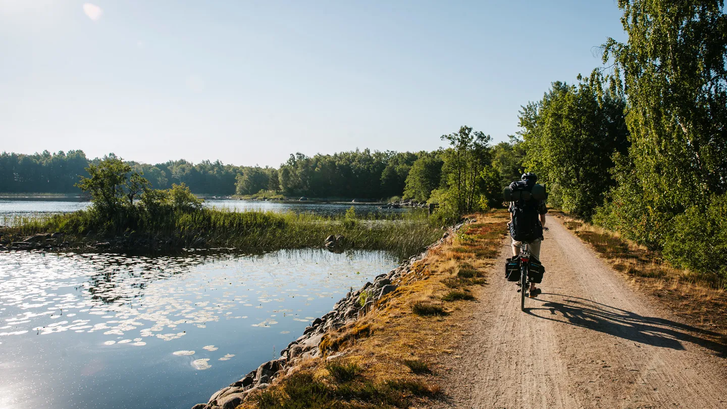 person cyklar på grusväg bredvid sjö
